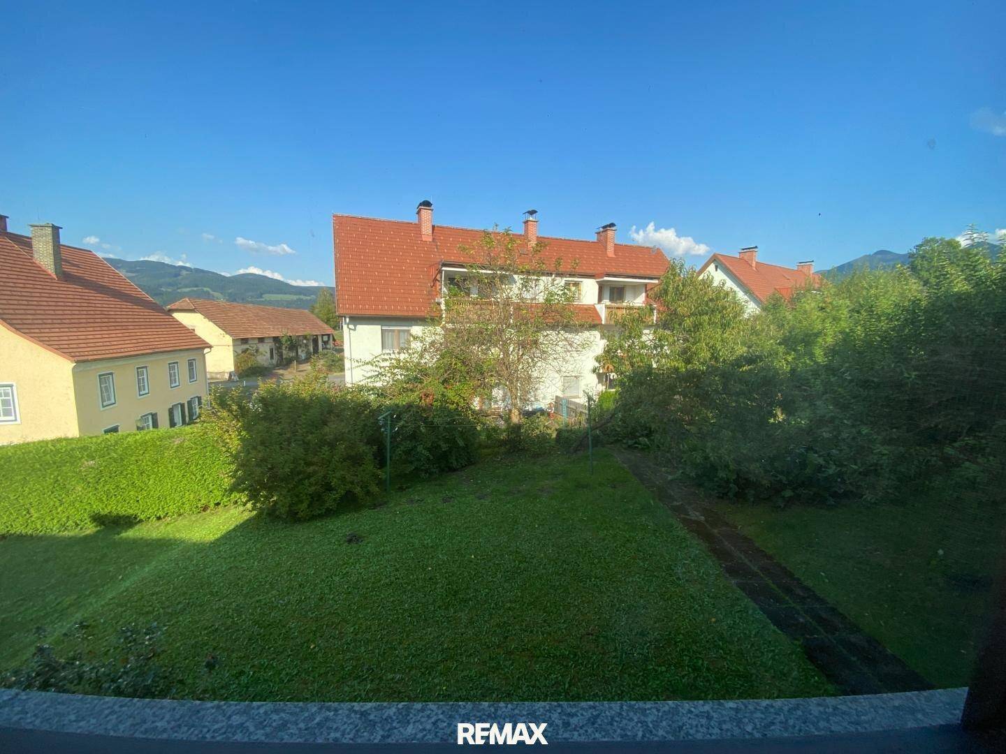 Weitläufiger Blick über grüne Hügel und Dächer benachbarter Häuser unter strahlend blauem Himmel.