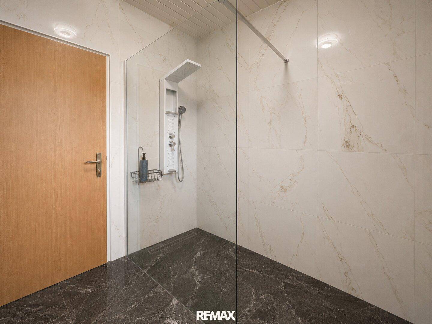 Modernes Badezimmer mit großformatigen Fliesen, begehbarer Dusche und Holztür.