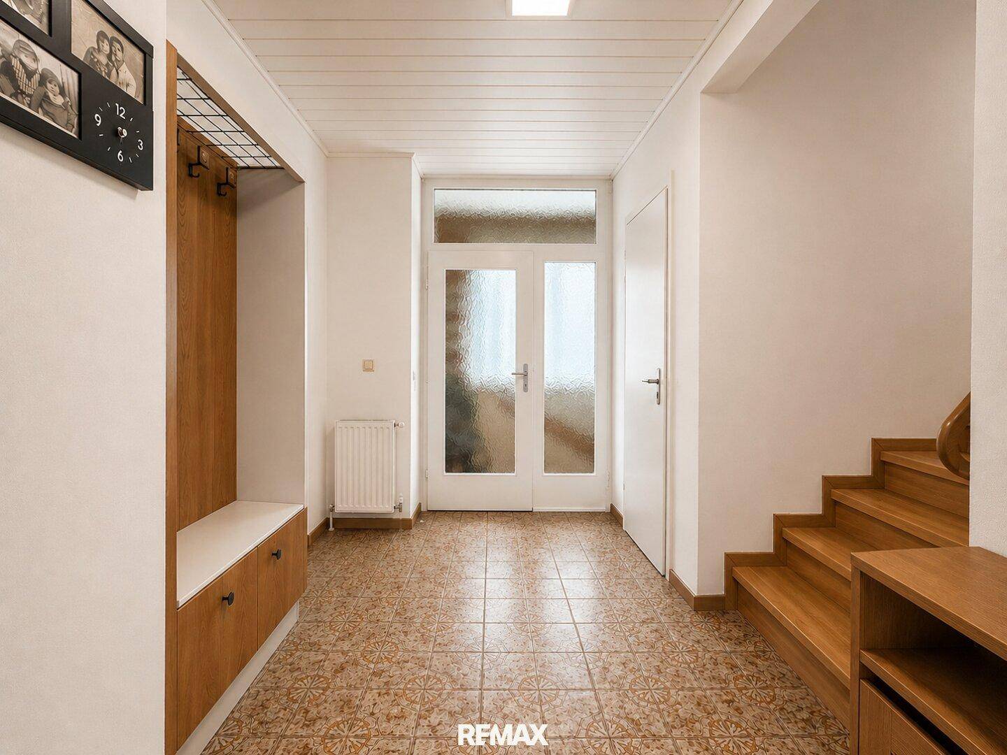 Heller Eingangsbereich mit Fliesenboden, Garderobe und Holztreppe zum Obergeschoss.