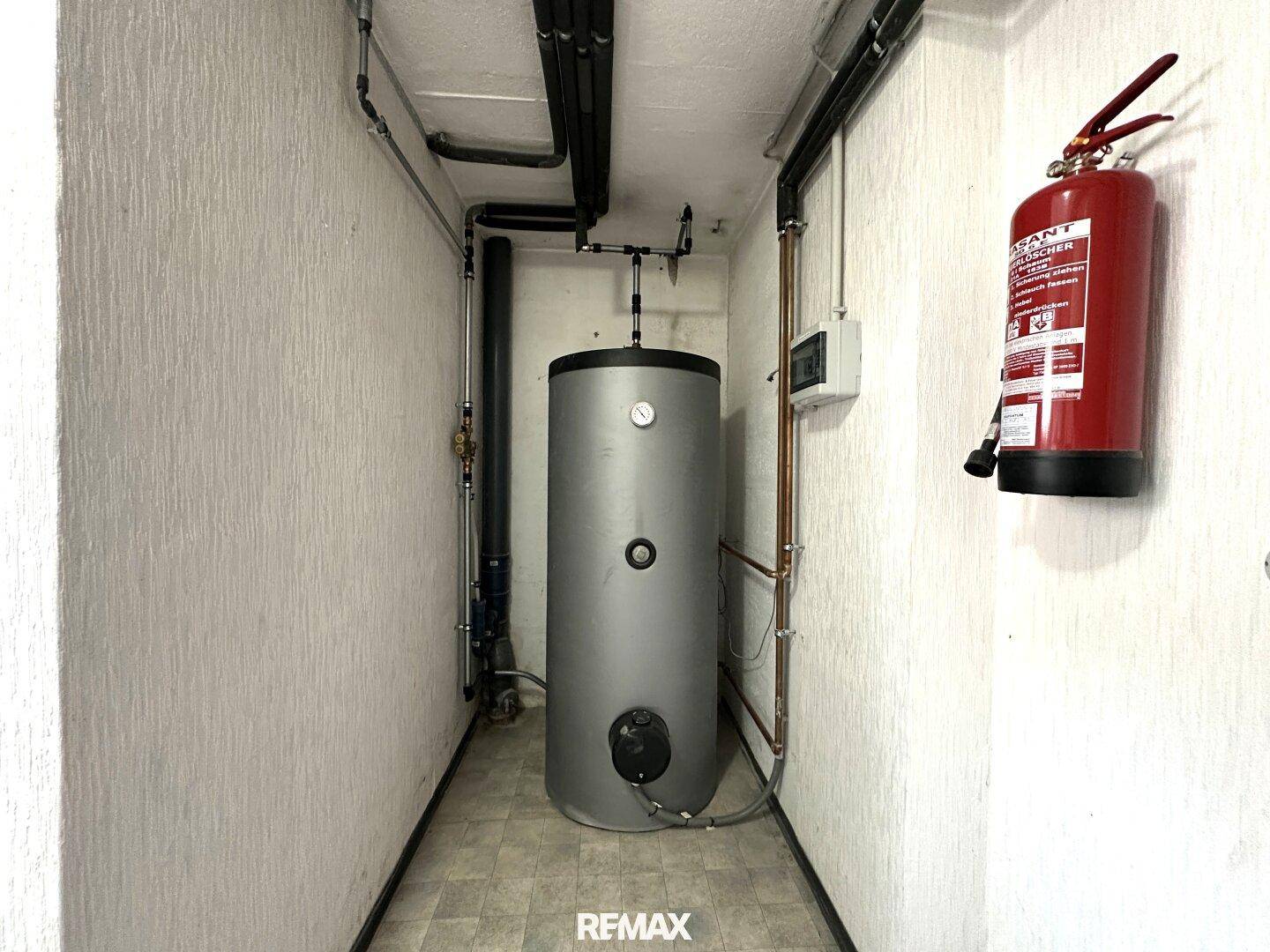 Heizungsraum mit Warmwasserspeicher, Rohren und Feuerlöscher.