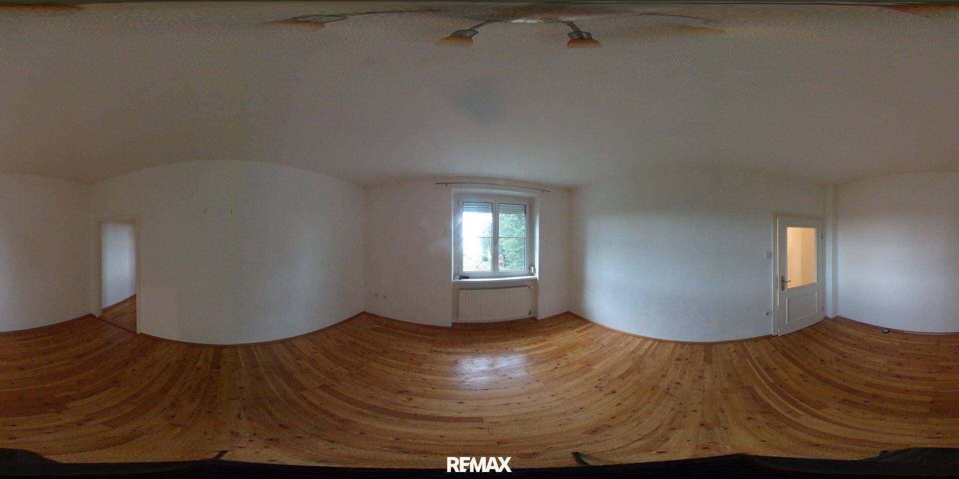 Panoramablick auf ein helles, leeres Wohnzimmer mit Holzboden und Fenster.