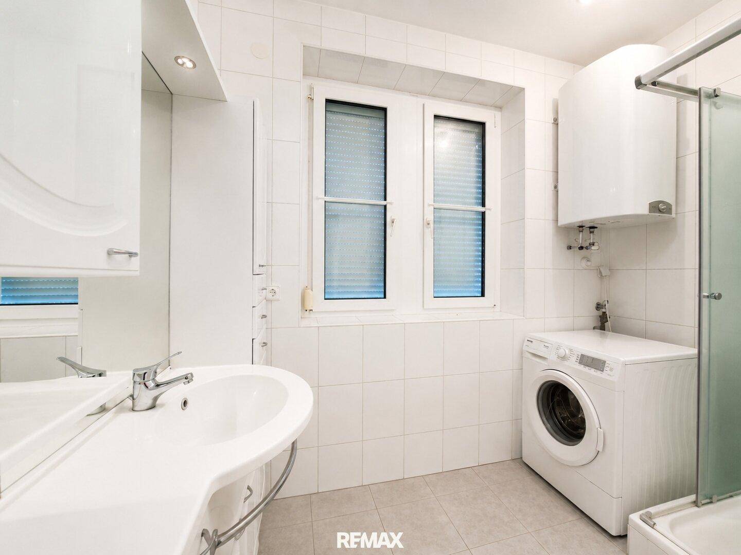 Gefliestes Badezimmer mit Dusche, Waschbecken, Waschmaschine und Warmwasserboiler.