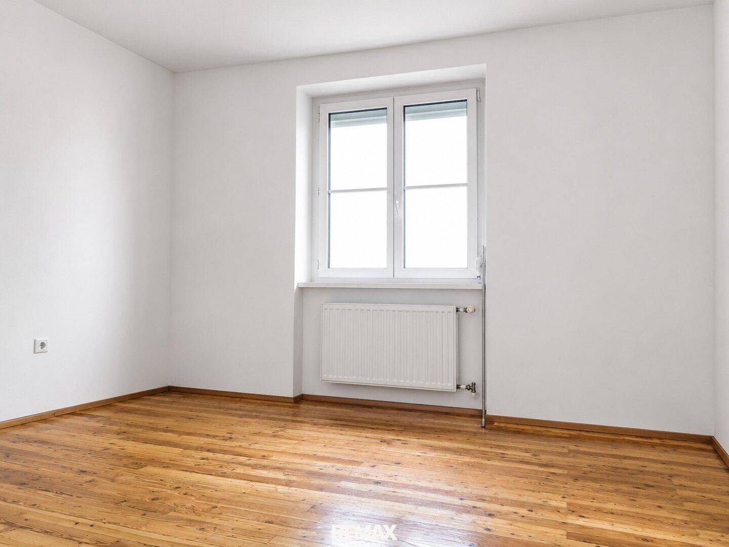 Leeres Schlafzimmer mit hellem Holzboden, weißen Wänden und einem Fenster.