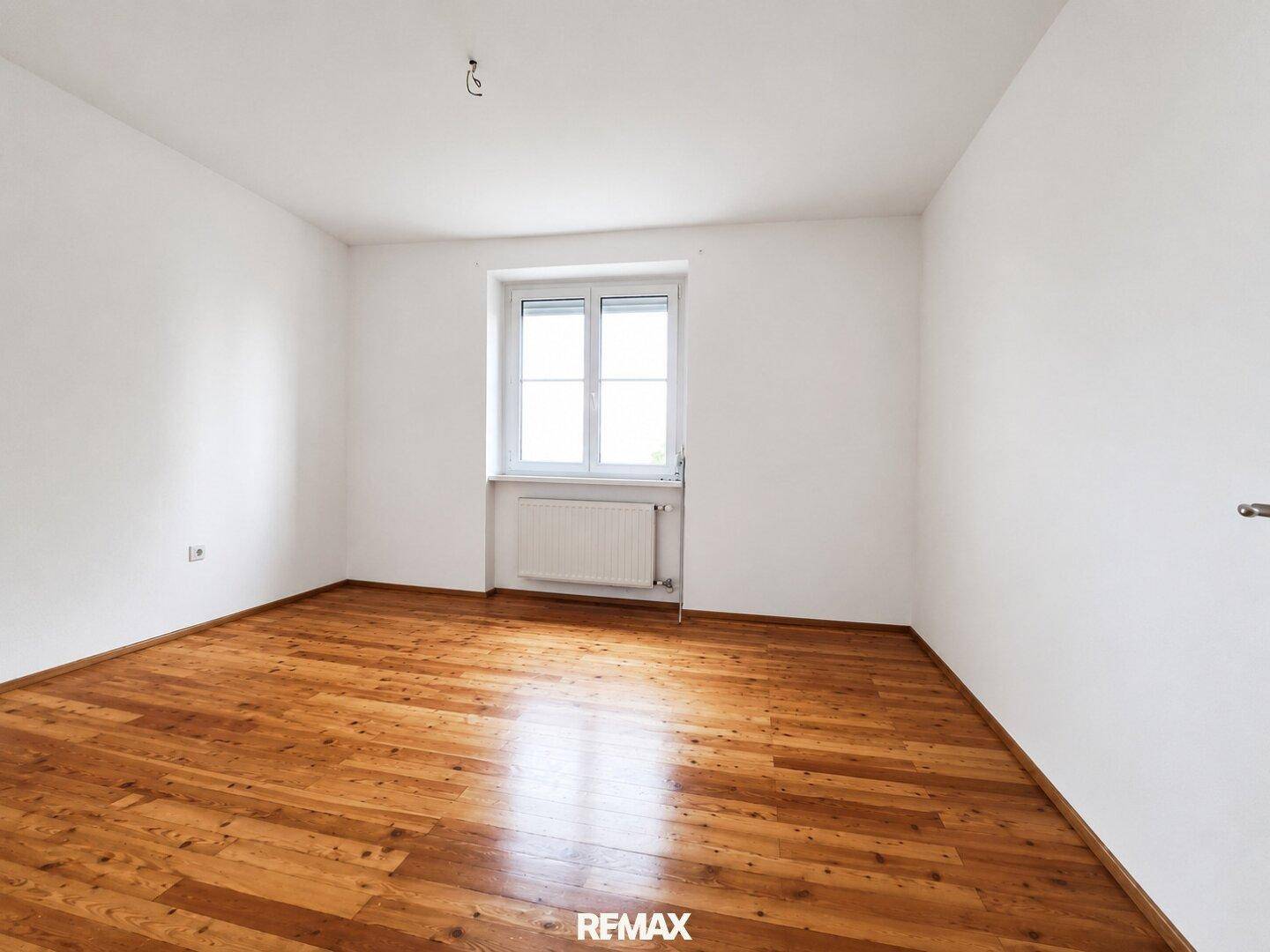 Geräumiges, leeres Zimmer mit Holzboden und weiß gestrichenen Wänden, bereit zur Einrichtung.