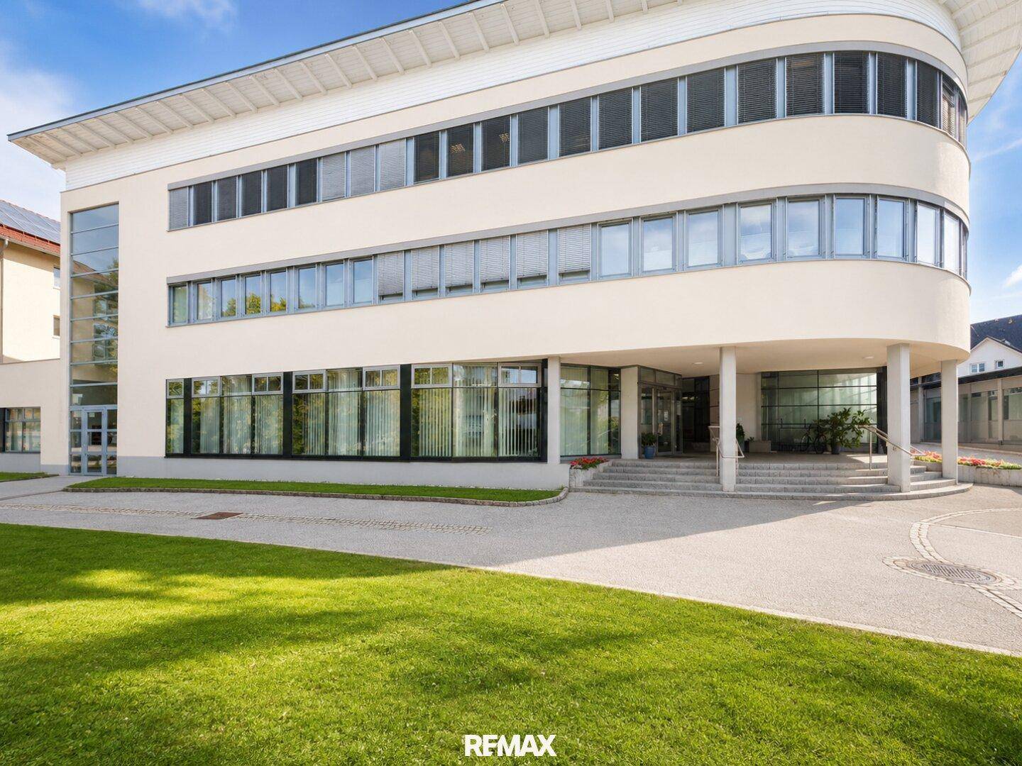 Elegante Fassade eines modernen Bürogebäudes mit großen Fenstern und Grünflächen.