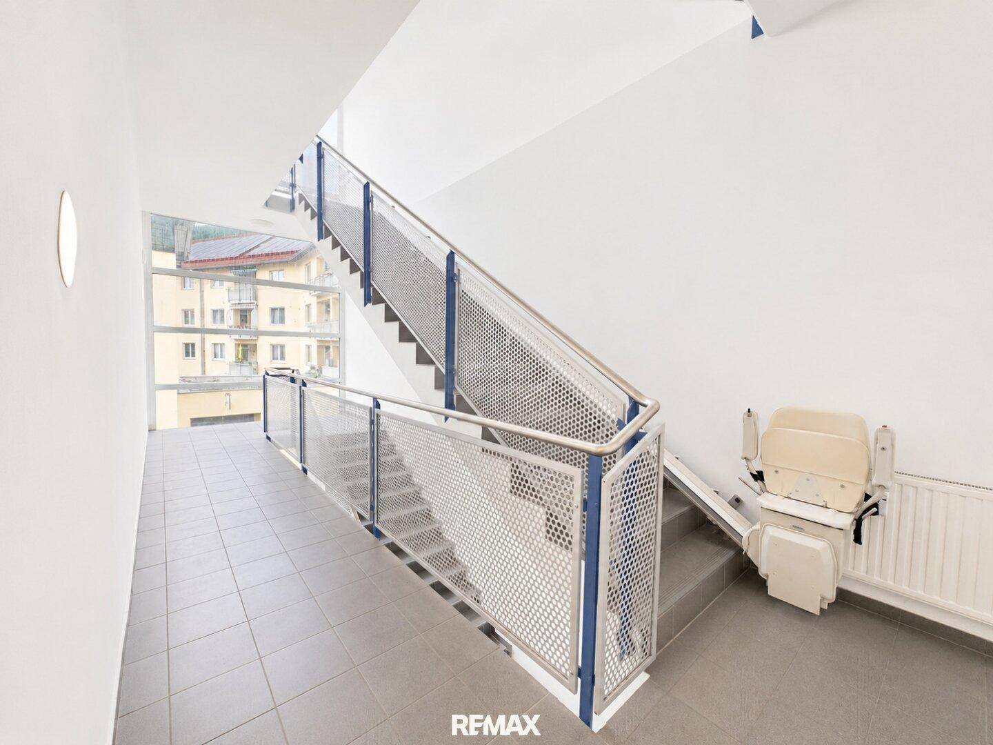 Treppenhaus mit Metallgeländer und installiertem Treppenlift für Barrierefreiheit.