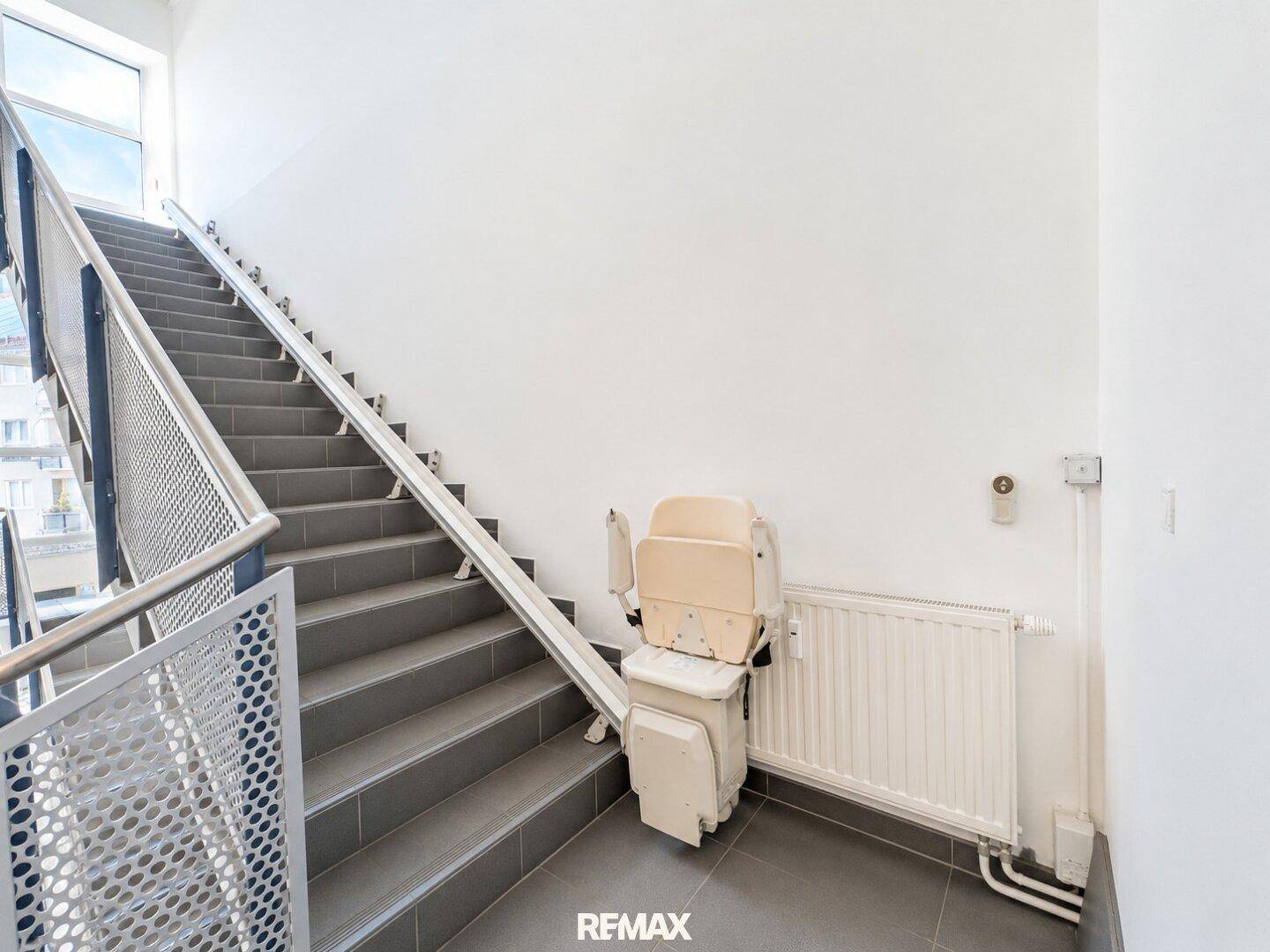 Geräumiges Treppenhaus mit Treppenlift und großen Fenstern für viel Tageslicht.
