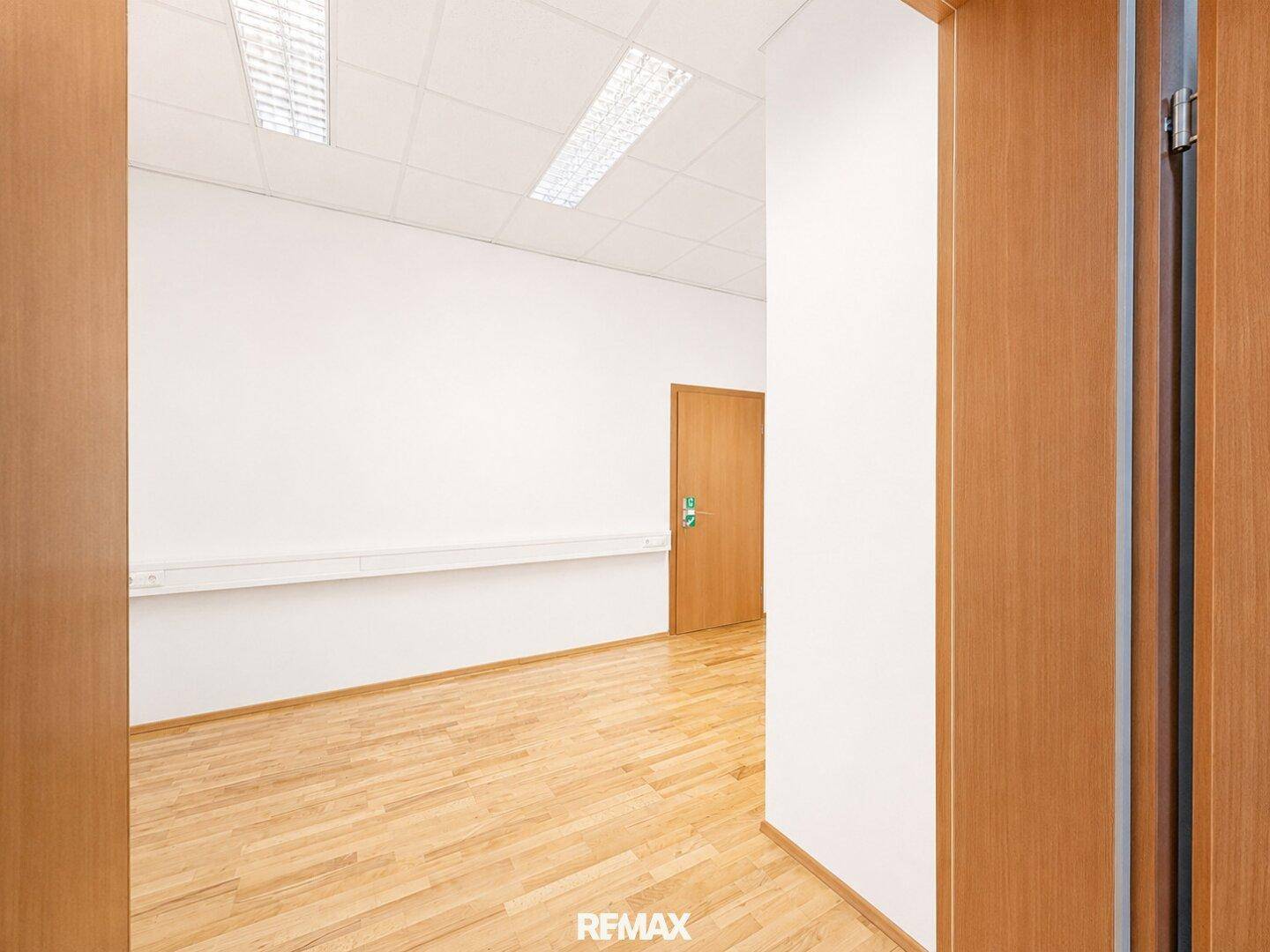 Eingangsbereich eines Bürozimmers mit hellem Holzfußboden und weißen Wänden.