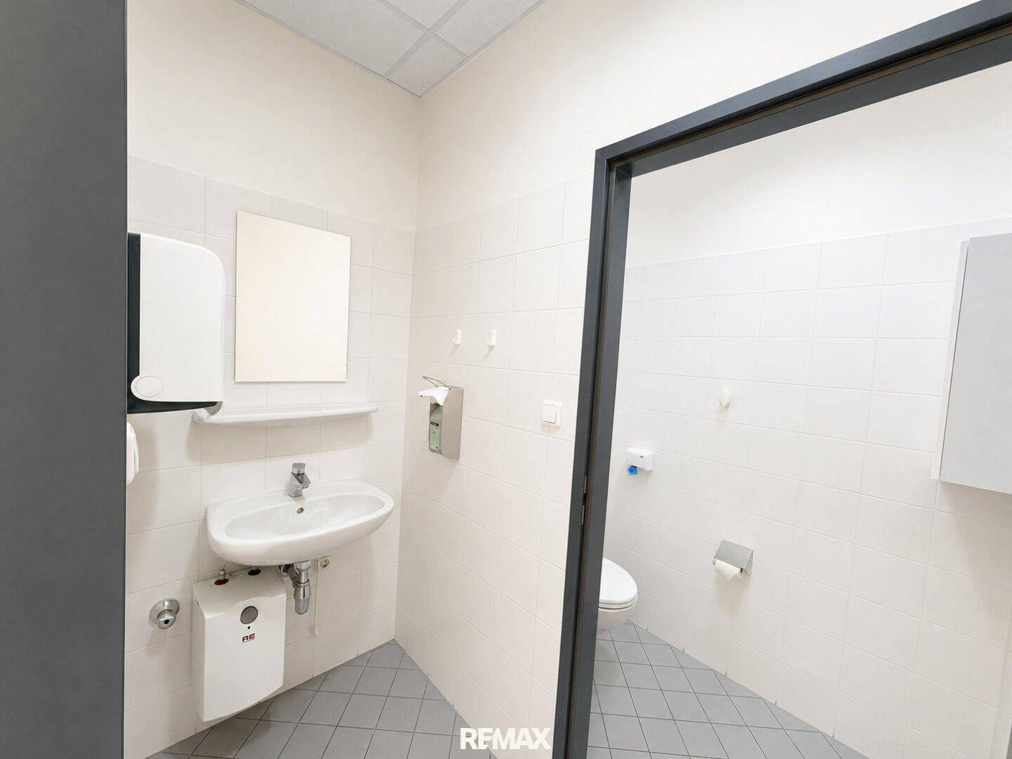 Helles WC mit Waschbecken, Spiegel und wandhängender Toilette, komplett gefliest.