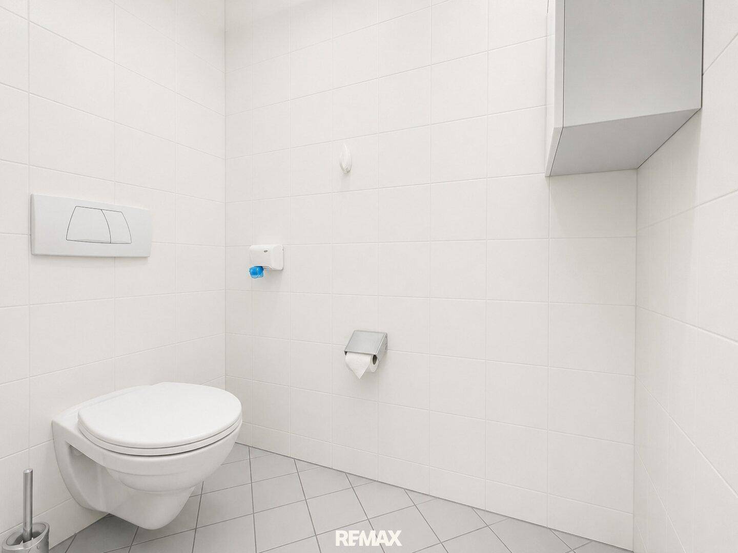 Modernes WC mit wandhängender Toilette und weißen Fliesen an Wänden und Boden.