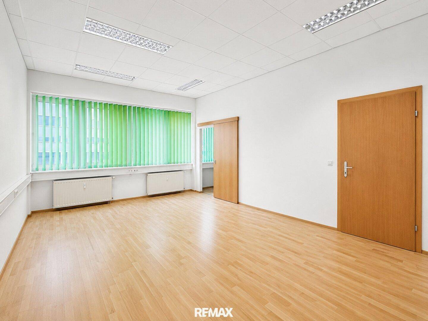 Helles Bürozimmer mit Holzparkett, großen Fenstern und Schiebetür zu einem weiteren Raum.