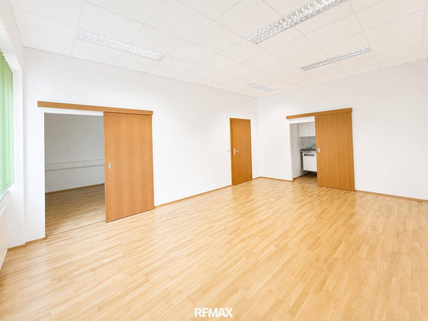 Geräumiges Bürozimmer mit Holzparkett und Zugang zu einer kleinen Küchenzeile.