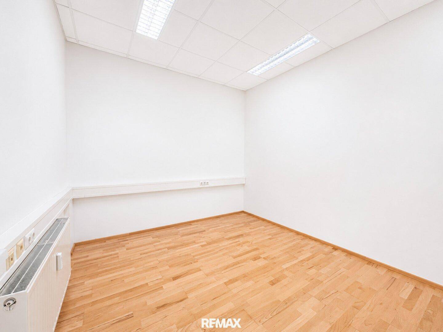 Kleineres Bürozimmer mit hellem Holzfußboden, weißen Wänden und Heizkörper.