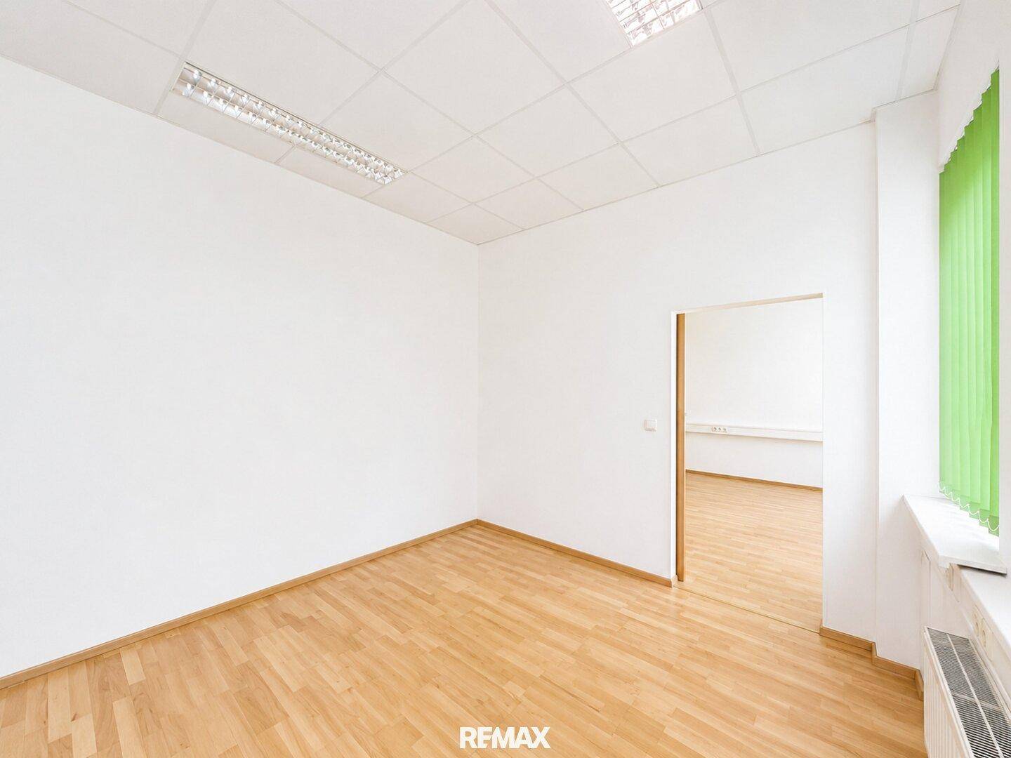 Helles Bürozimmer mit Holzparkett und Blick in einen weiteren Raum durch die Türöffnung.