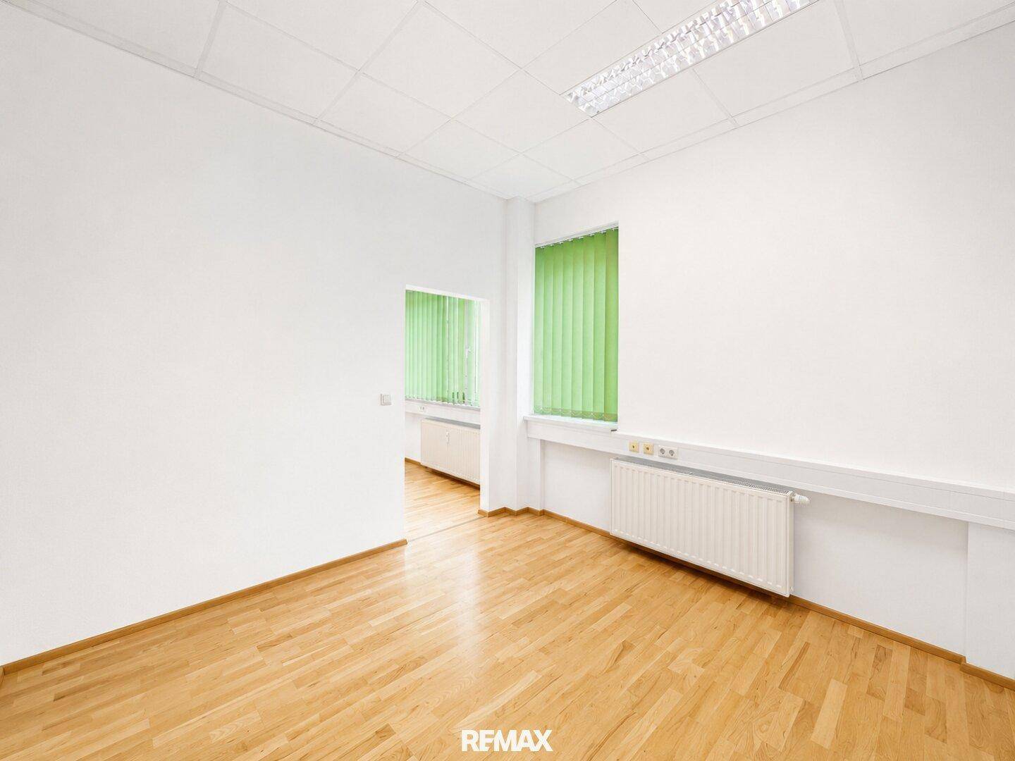 Bürozimmer mit hellem Holzfußboden und Blick auf eine kleine Küchenzeile.