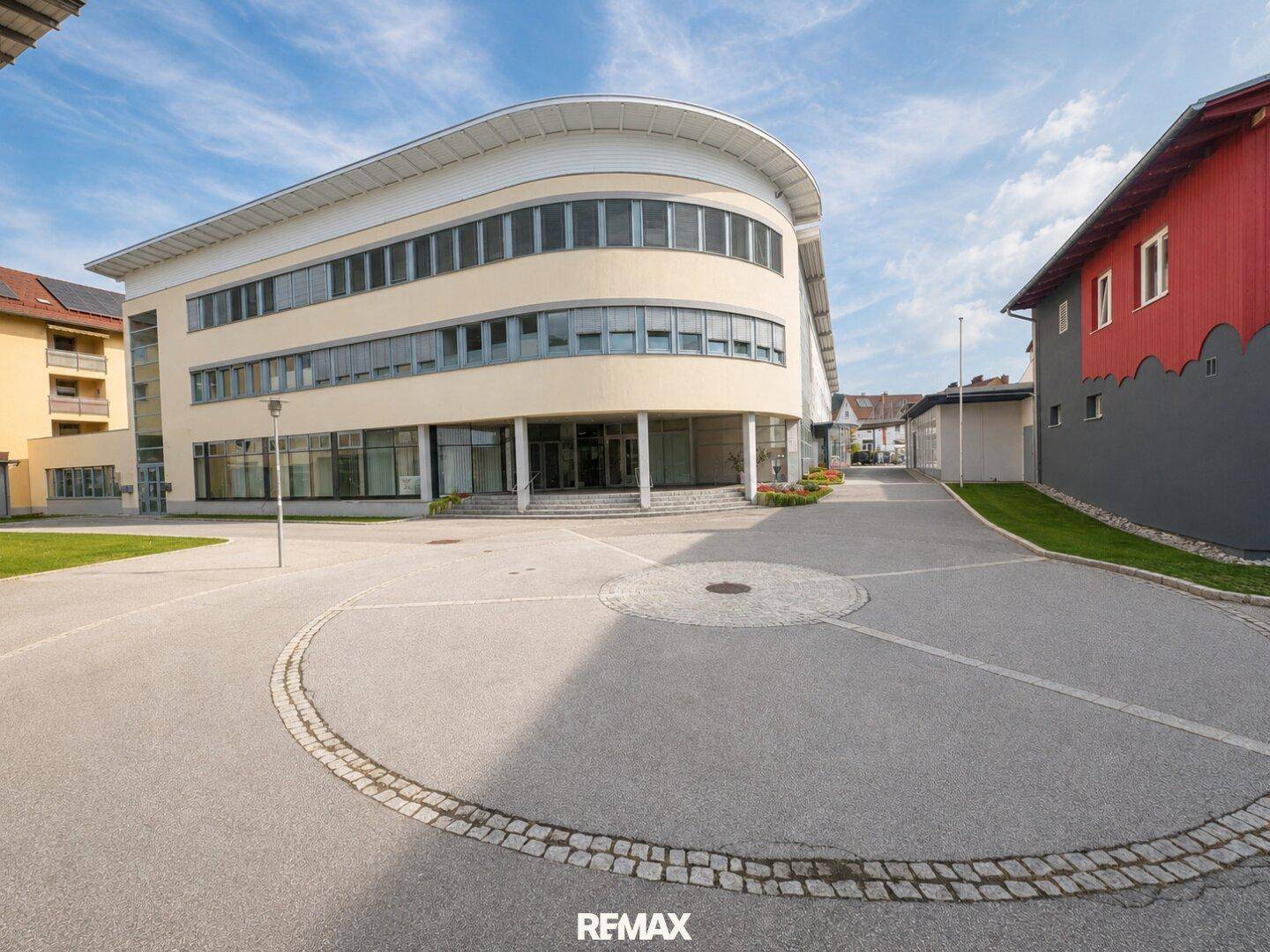Außenansicht eines modernen Bürogebäudes mit geschwungener Architektur und großzügiger Zufahrt.