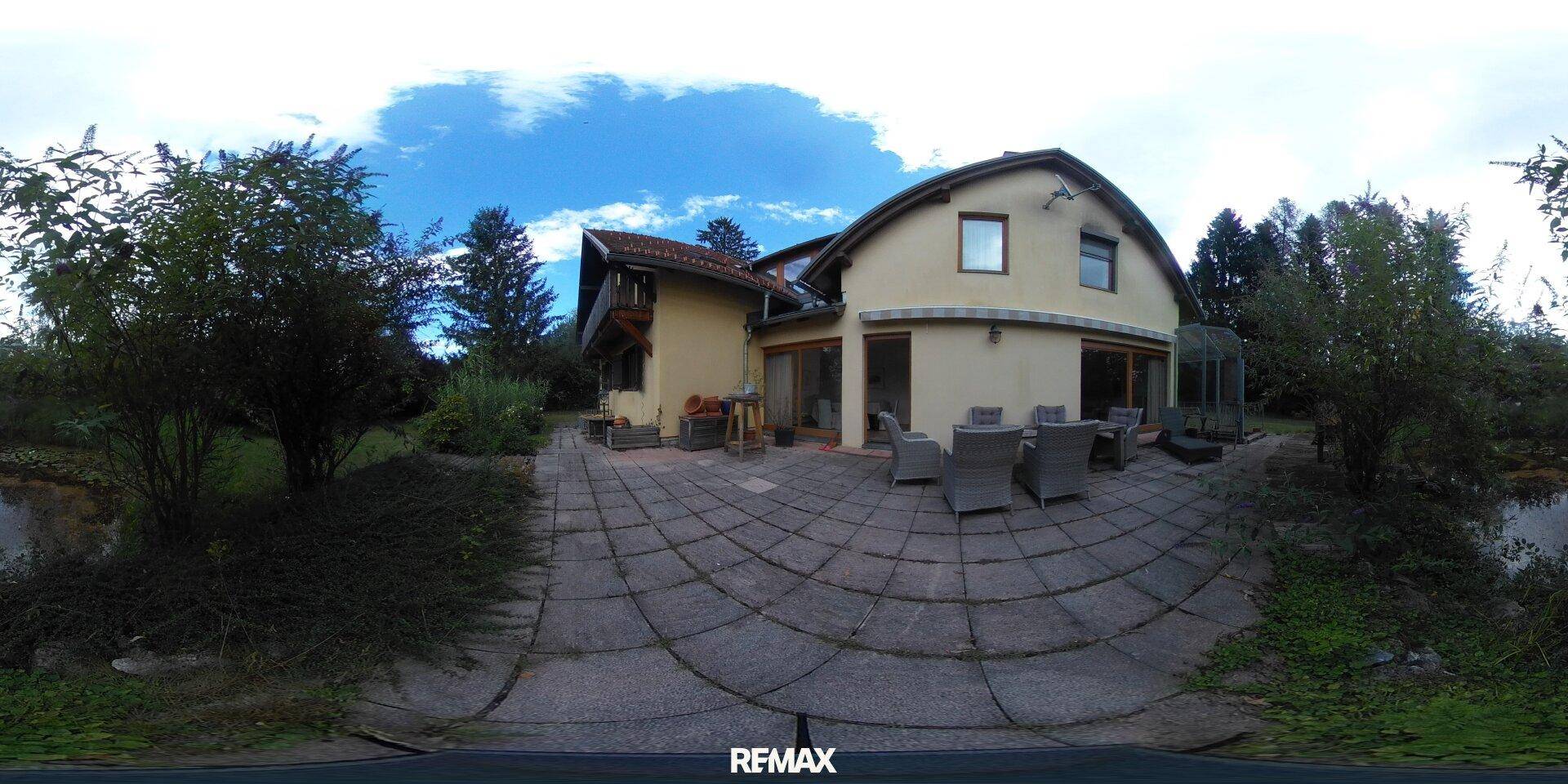 Große gepflasterte Terrasse mit Gartenmöbeln hinter dem Haus, umgeben von viel Grün.