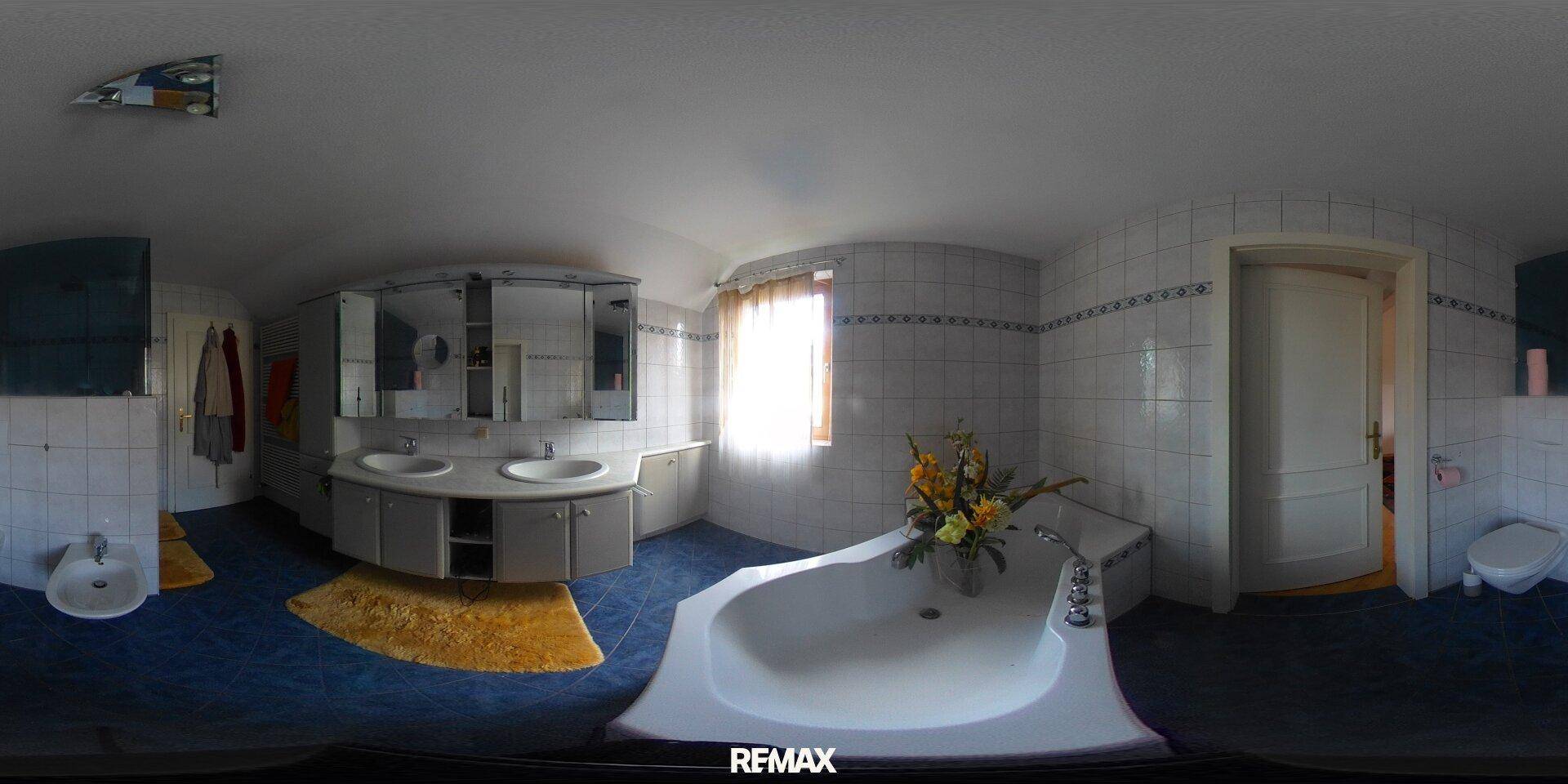 Badezimmer mit blauen Fliesen, Doppelwaschbecken und einer Eckbadewanne unter dem Fenster.