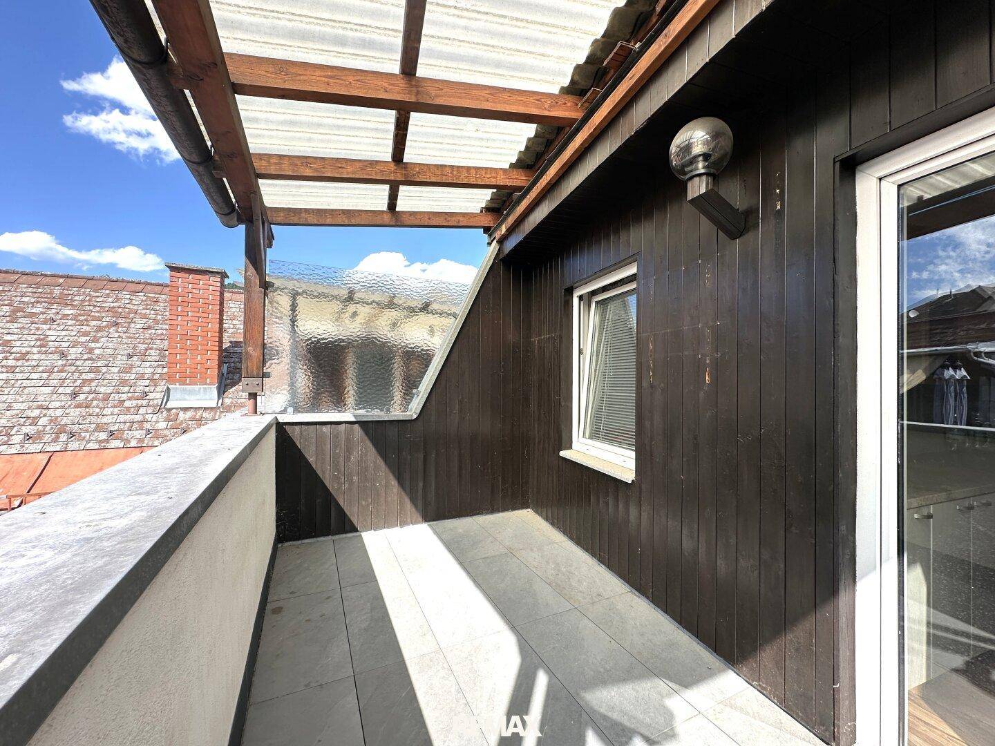 Überdachter Terrassenbereich mit Holzelementen und Fliesenboden, bietet einen geschützten Außenbereich.