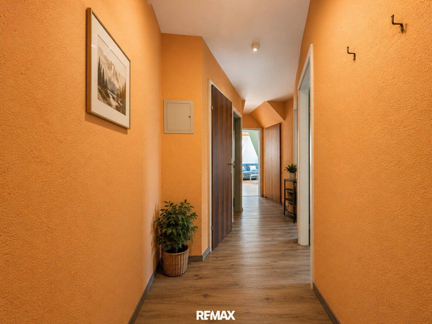 Heller Flur mit auffälligen orangefarbenen Wänden und Laminatboden, führt zu weiteren Räumen.