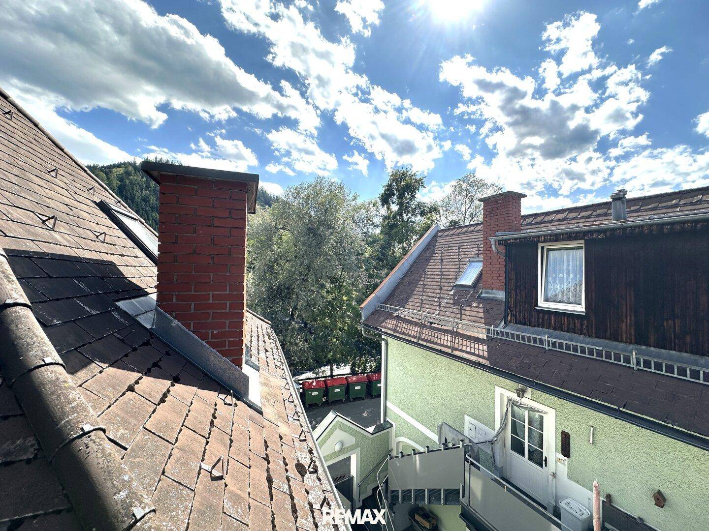 Blick über die Dächer der umliegenden Gebäude mit Schornsteinen und grünen Bäumen.