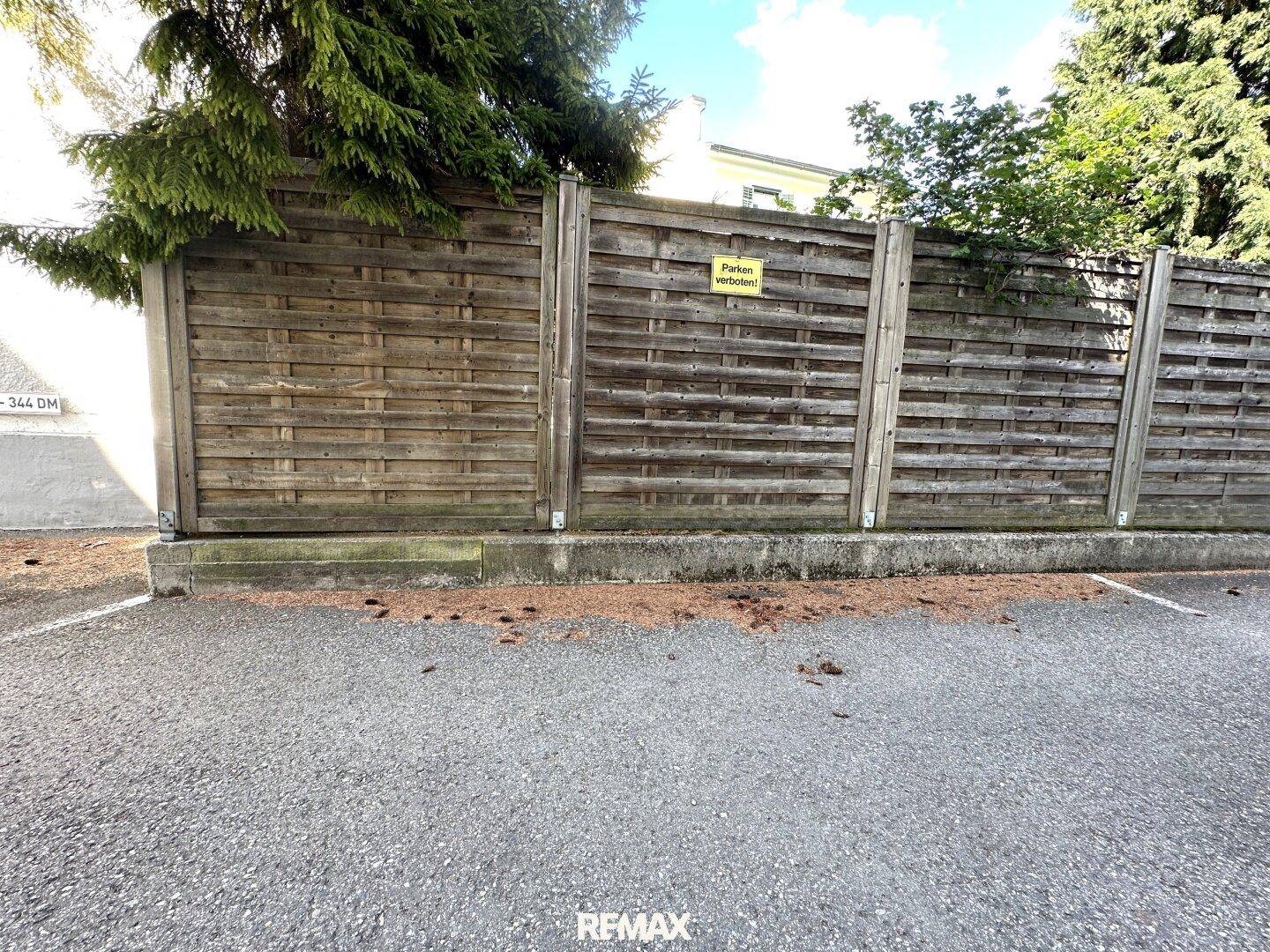 Holzzaun neben einem gepflasterten Parkplatz mit einem "Parken verboten!" Schild.