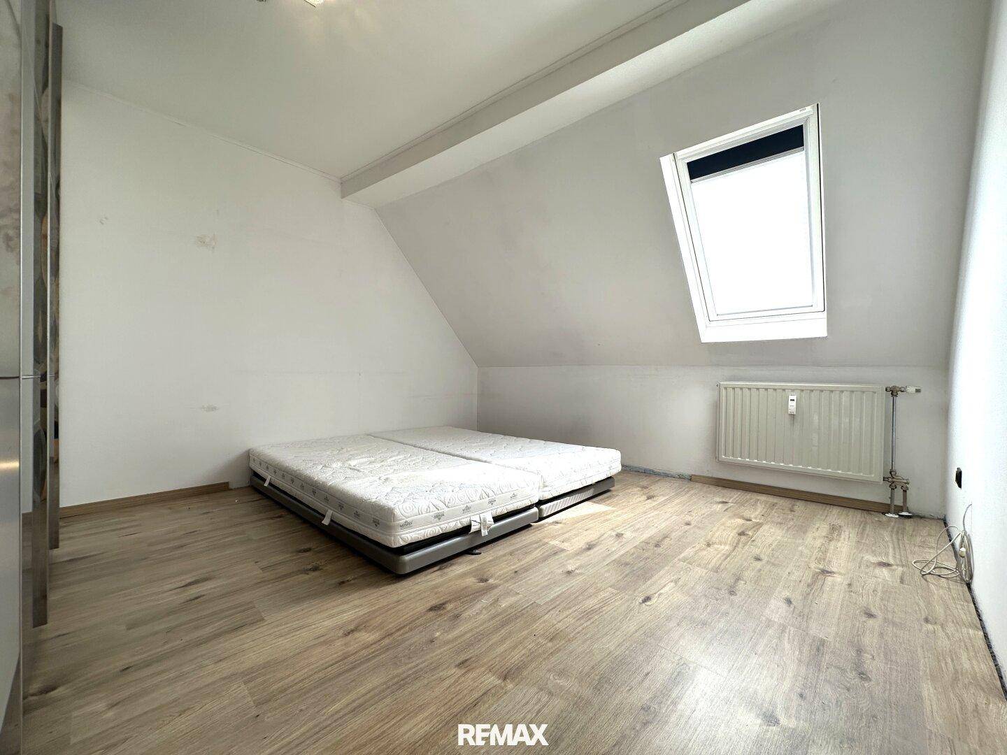 Schlafzimmer mit Matratze auf dem Boden, Heizkörper und einem Dachfenster für natürliches Licht.