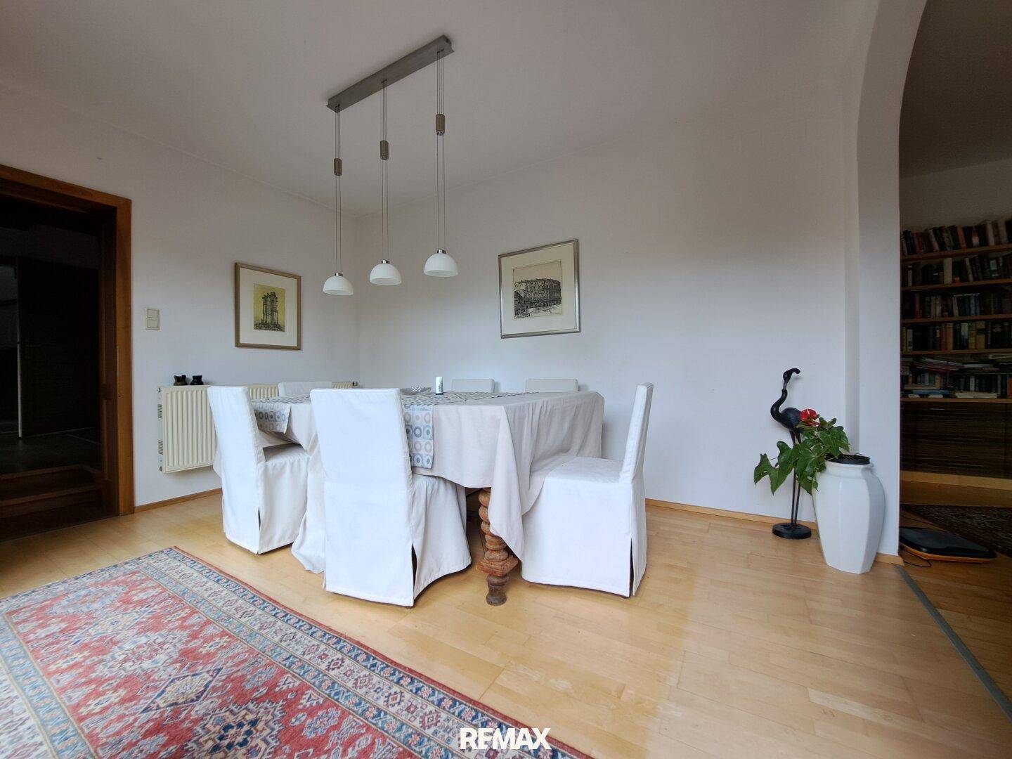 Eleganter Essbereich mit großem Tisch, weißen Stühlen und Parkettboden.