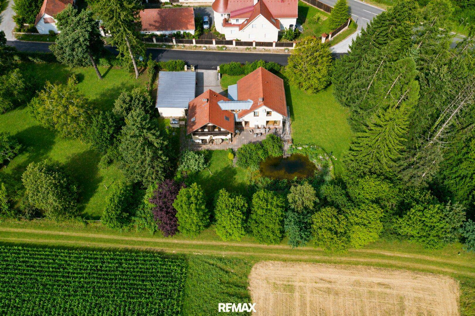 Luftaufnahme des Anwesens mit großem Garten, Teich und angrenzenden Feldern.