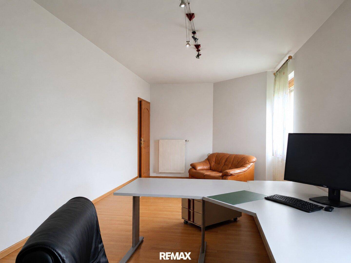 Helles Arbeitszimmer mit Schreibtisch, Bürostuhl und Parkettboden.