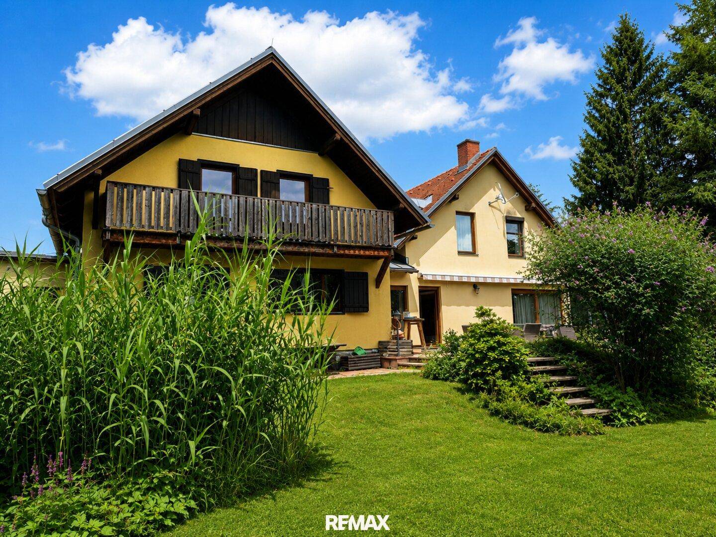 Rückseite des Hauses mit Balkon, umgeben von einem gepflegten Garten und hohen Gräsern.