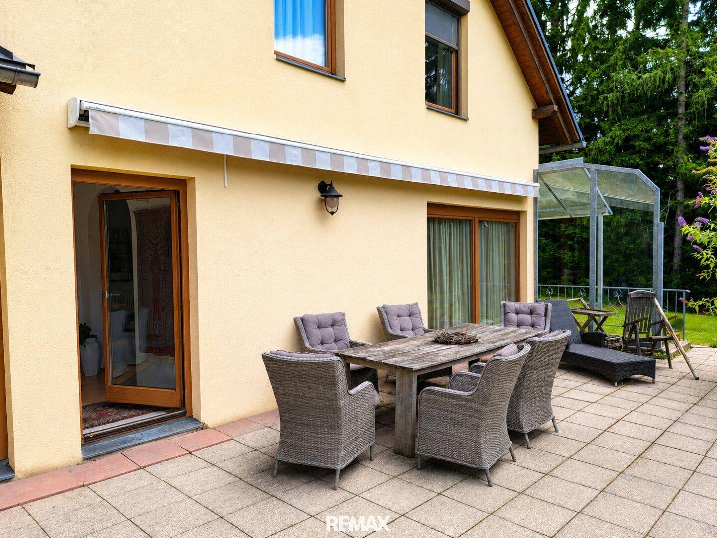 Geräumige Terrasse mit Holztisch und Korbstühlen, geschützt durch eine Markise.