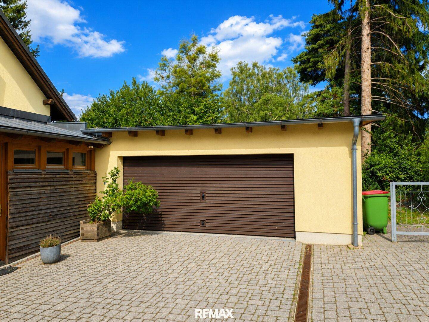 Externe Garage mit braunem Rolltor und gepflasterter Zufahrt neben dem Haus.