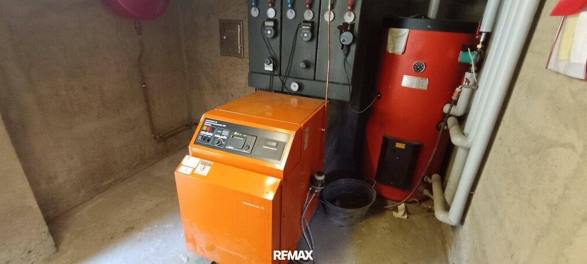 Heizungsraum mit einem orangefarbenen Heizkessel und Warmwasserspeicher.