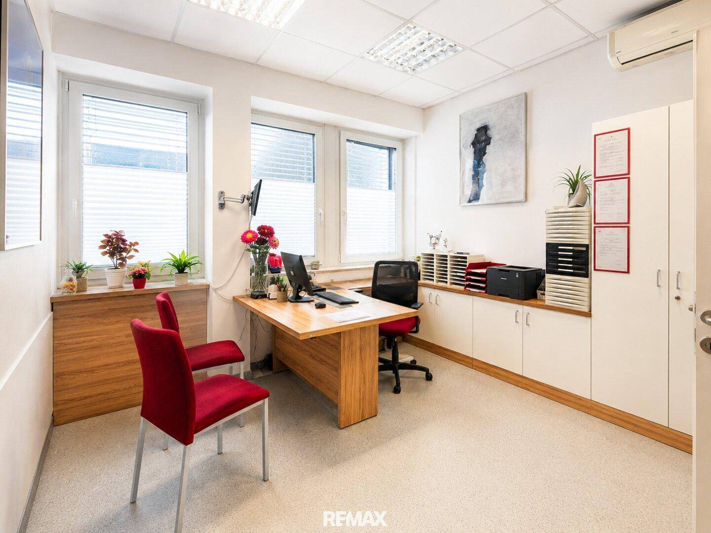 Helles Büro mit Holzschreibtisch, roten Stühlen und praktischen Einbauschränken für eine effiziente Arbeitsumgebung.