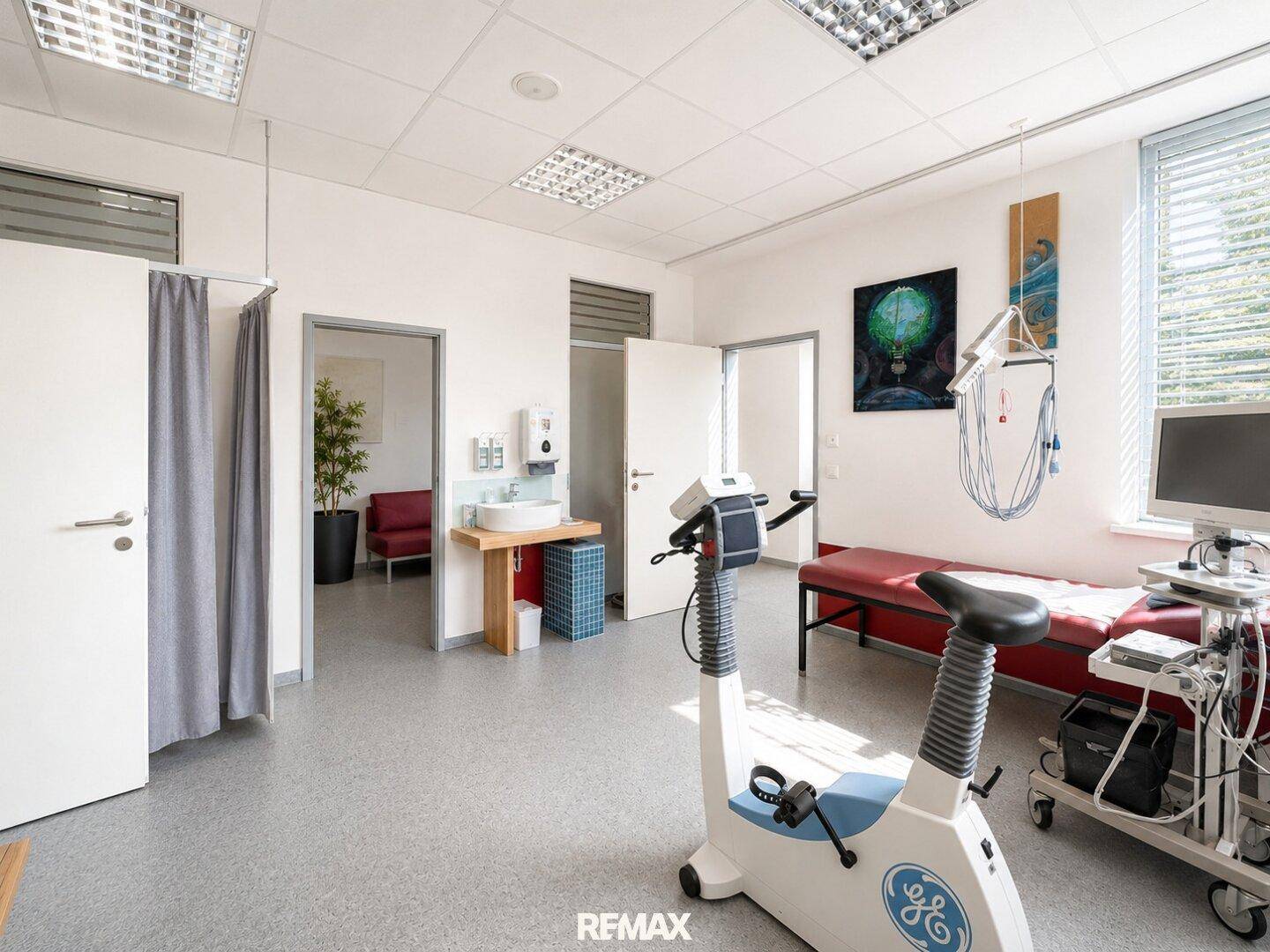 Behandlungsraum mit Ergometer, Waschbecken und Zugang zu weiteren Bereichen.