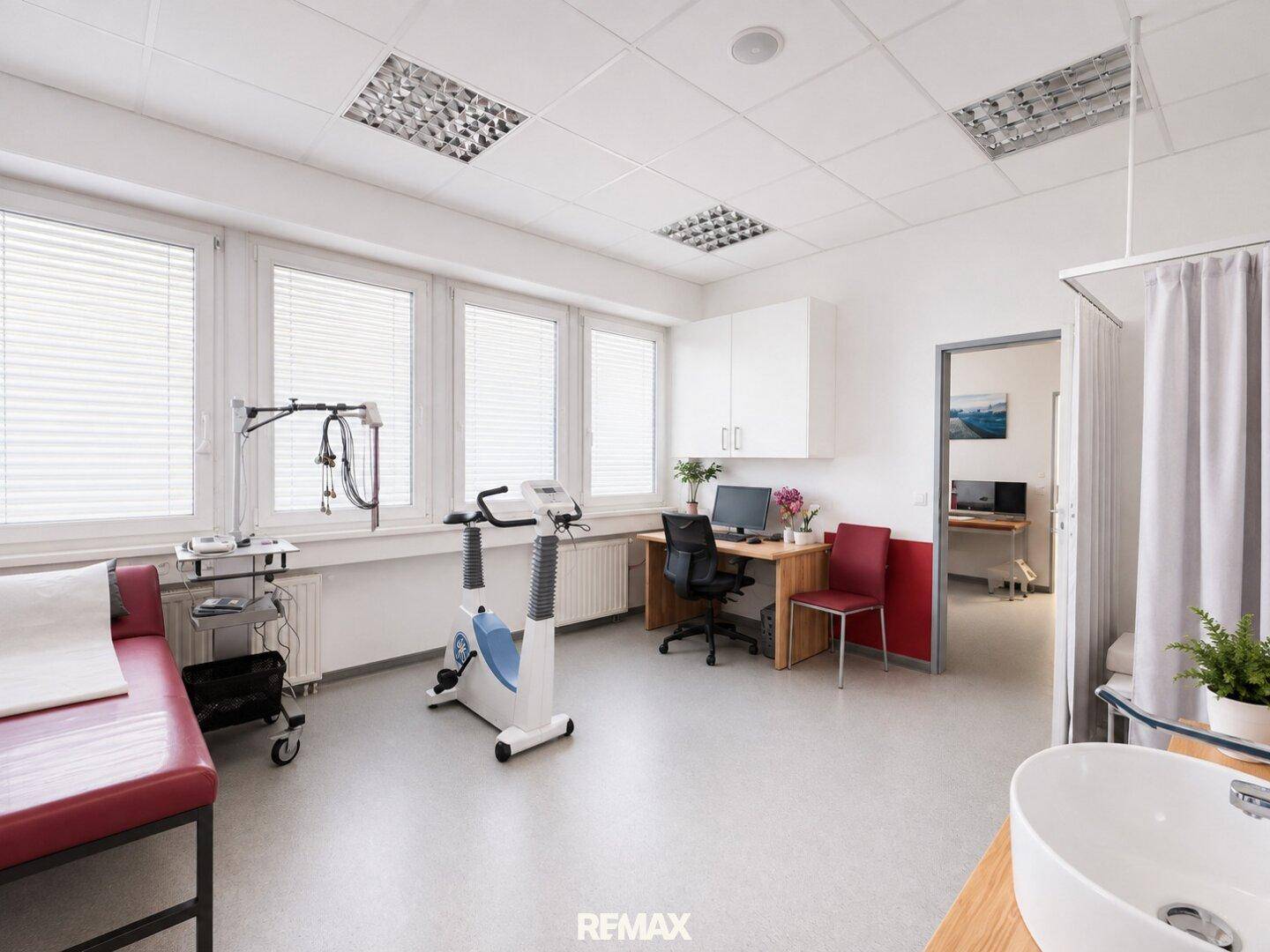 Heller Behandlungsraum mit Untersuchungsliege, Ergometer und Schreibtisch.
