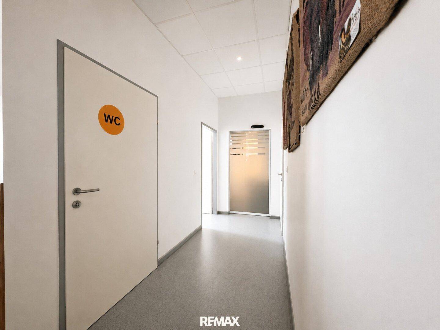 Heller Flur mit WC-Beschilderung und moderner Glastür am Ende.