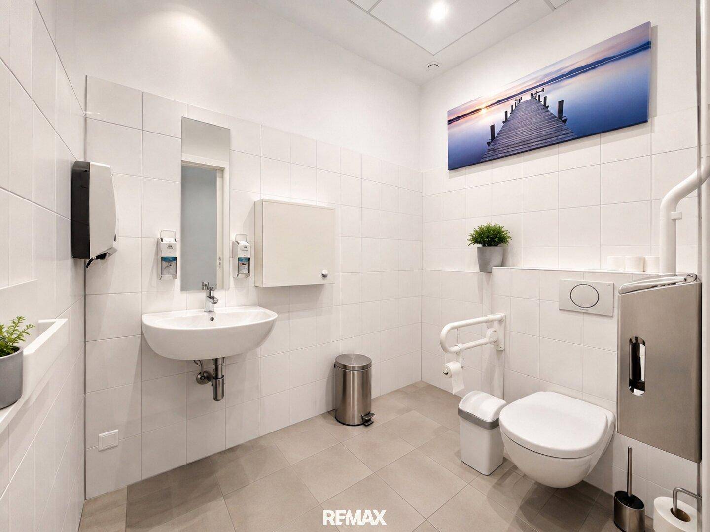 Barrierefreies WC mit weißen Fliesen, Waschbecken und Haltegriffen.