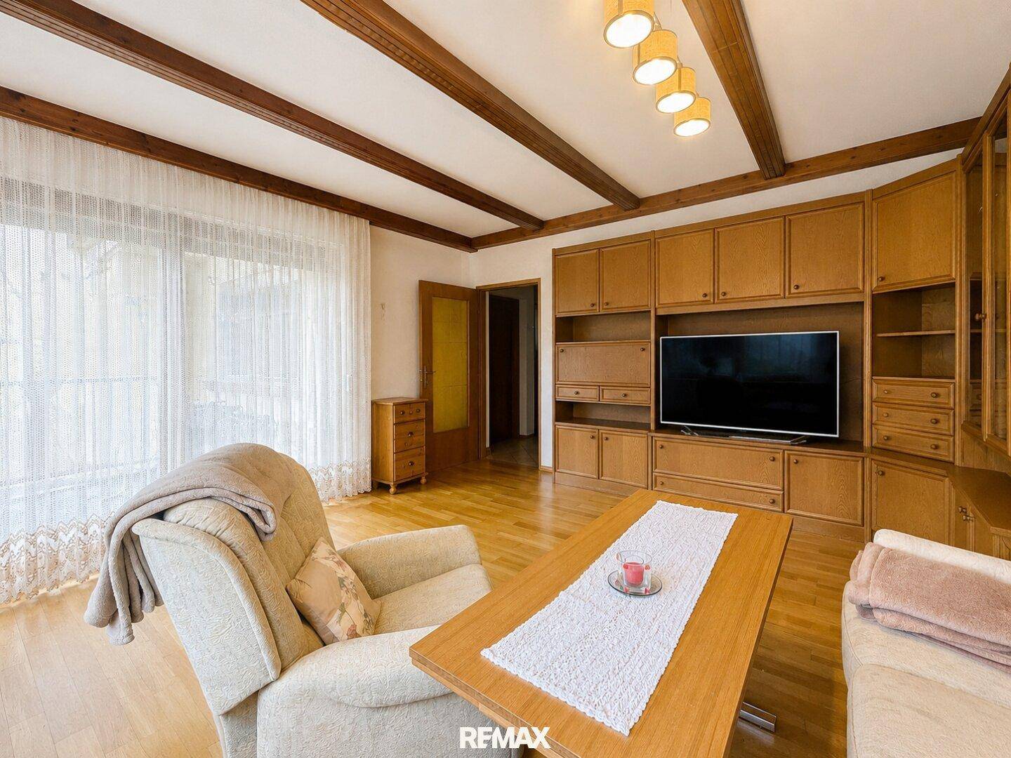 Wohnzimmer mit großer Holzschrankwand, Parkettboden und sichtbaren Deckenbalken.