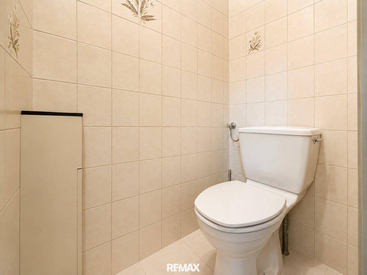 Gäste-WC mit hellen Fliesen an Wänden und Boden sowie einer Standardtoilette.