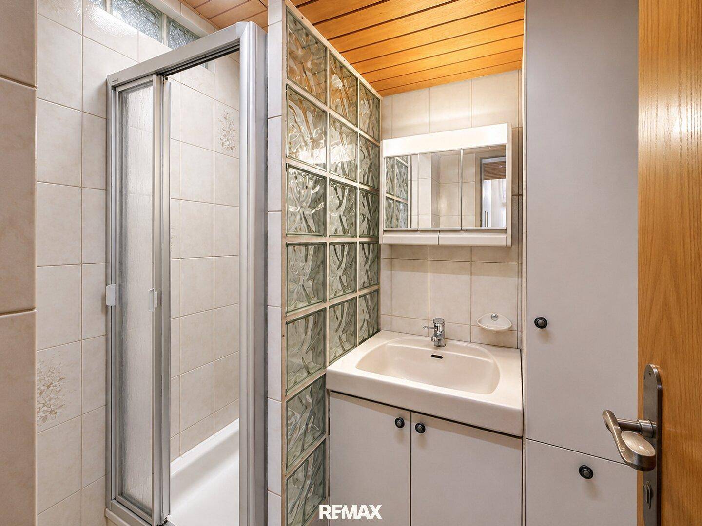 Badezimmer mit Duschkabine, Waschbecken, Spiegelschrank und Glasbausteinen.