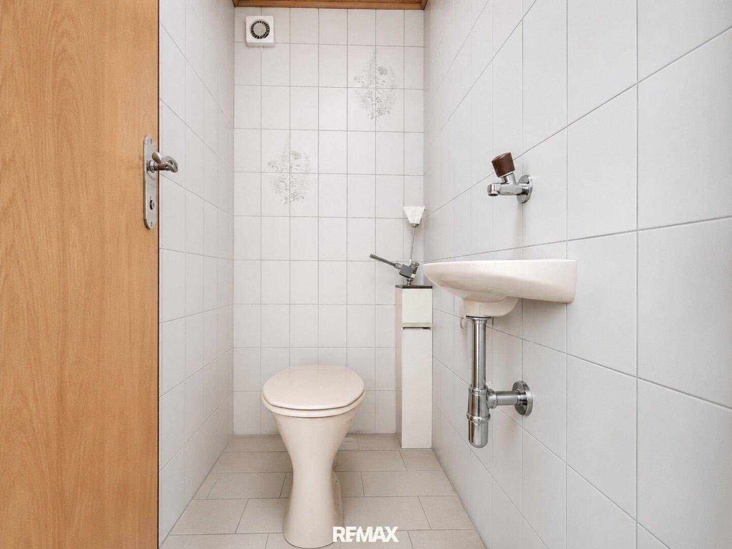Kleines Gäste-WC mit weißen Fliesen, Toilette und einem kompakten Waschbecken.