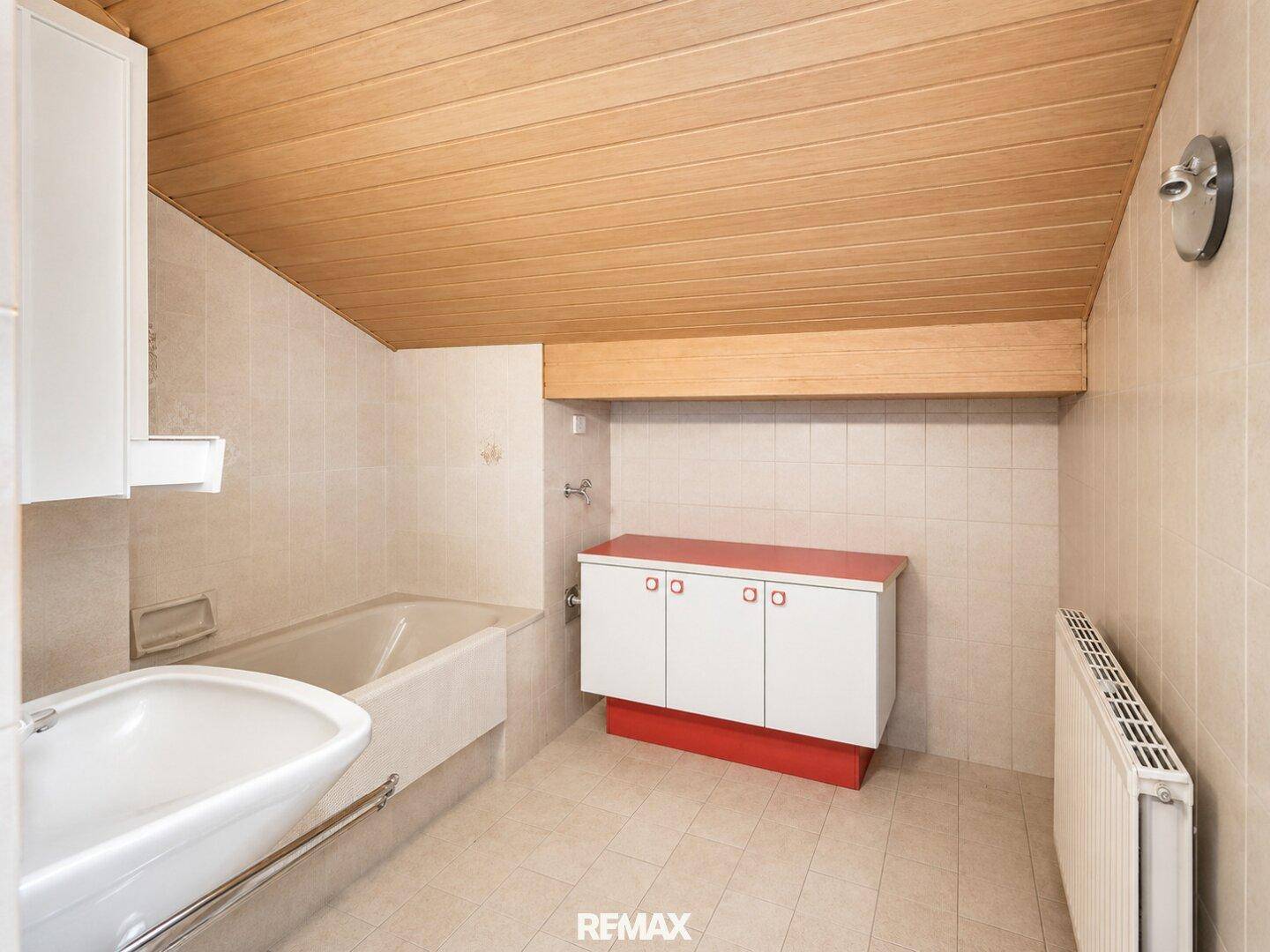Badezimmer mit Badewanne, Waschbecken, Holzdecke und schrägen Wänden im Dachgeschoss.