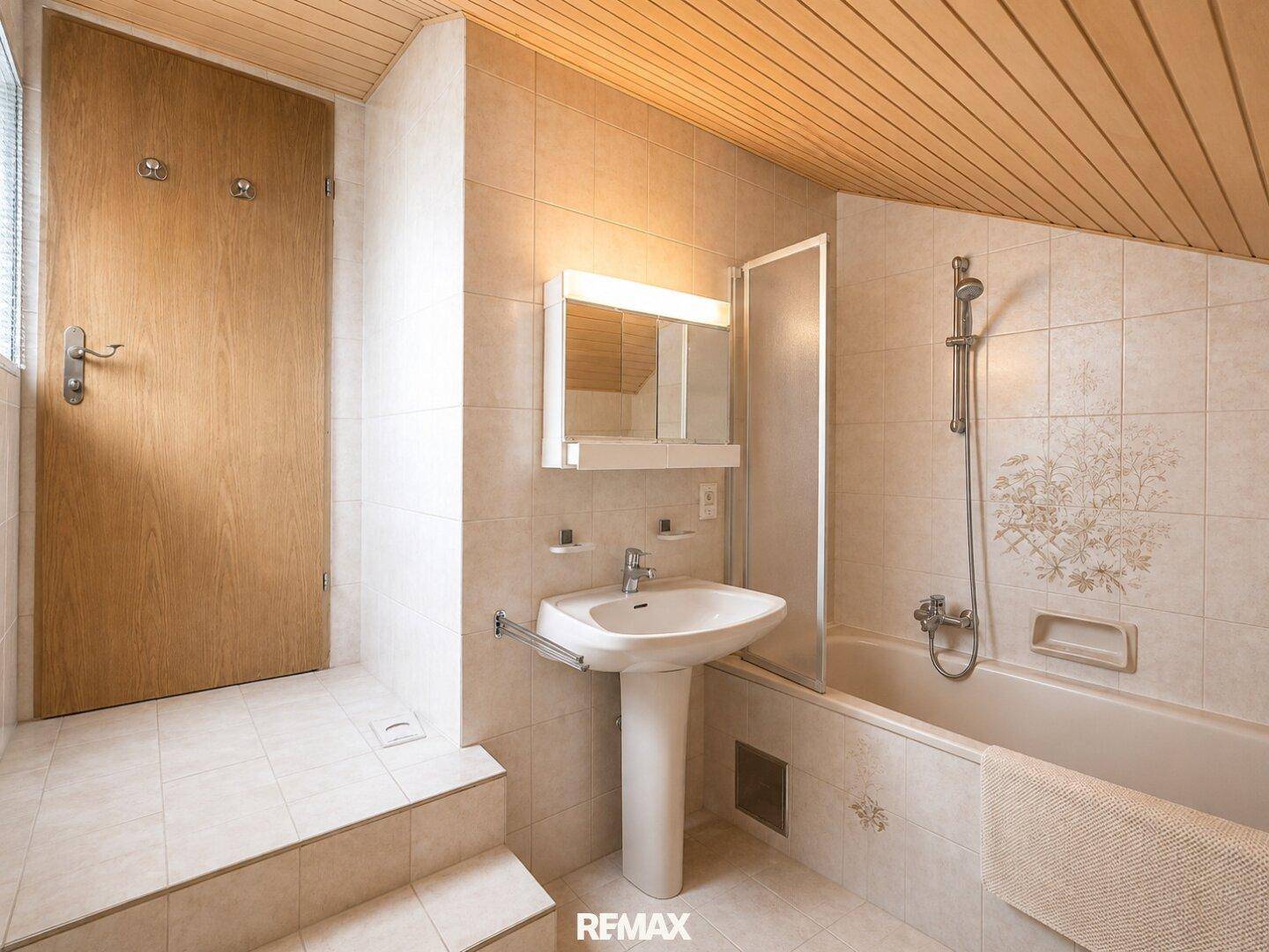 Badezimmer mit Badewanne, Duschfunktion, Standwaschbecken und Holzdecke.
