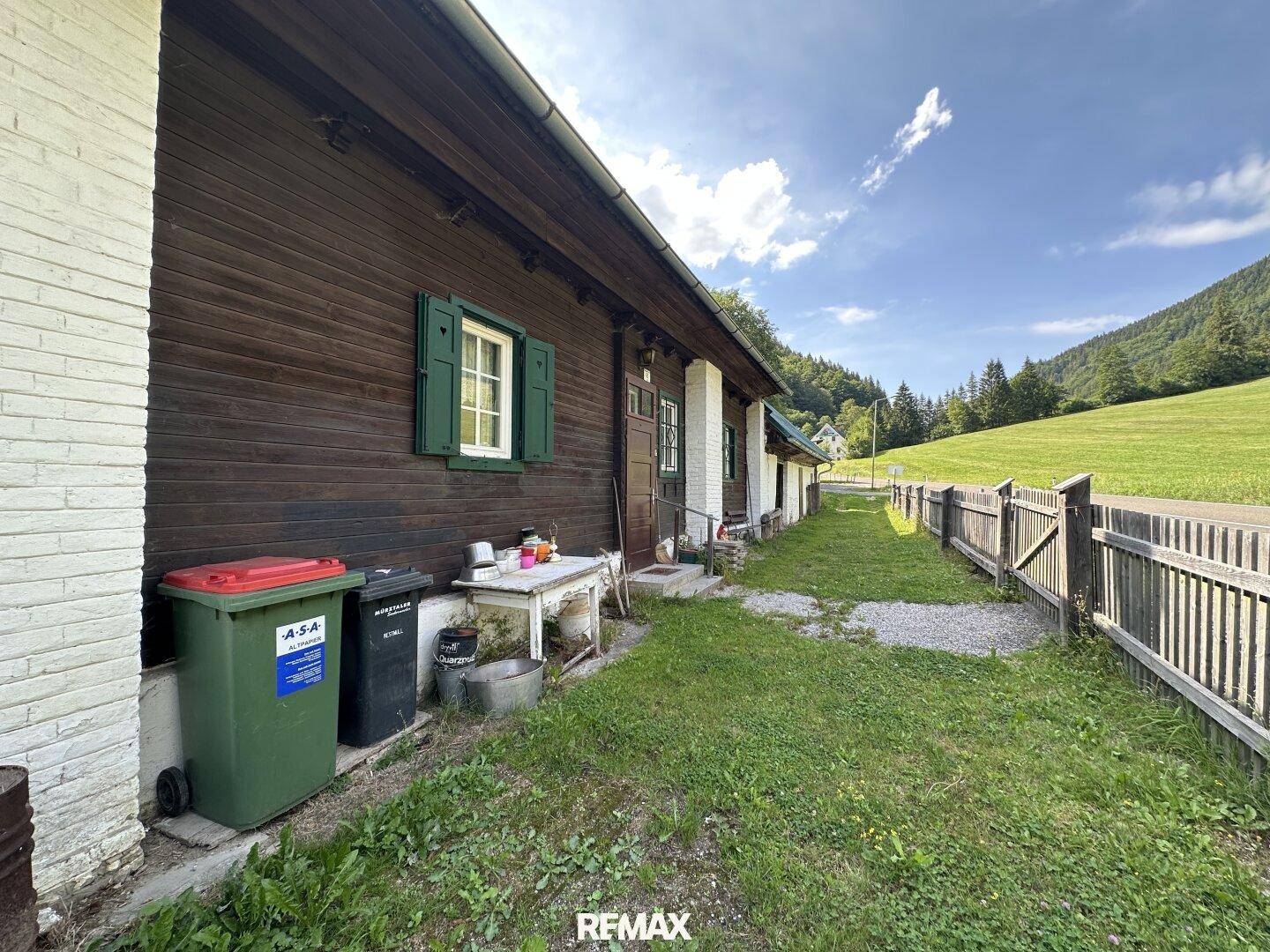 Seitenansicht des Hauses mit Eingangsbereich, Mülltonnen und Blick auf die grüne Umgebung.