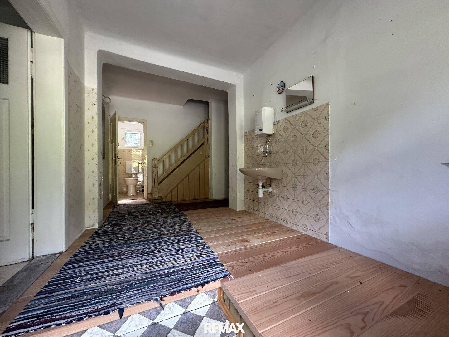 Eingangsbereich mit Holztreppe, Waschbecken und gefliestem Boden in traditionellem Stil.