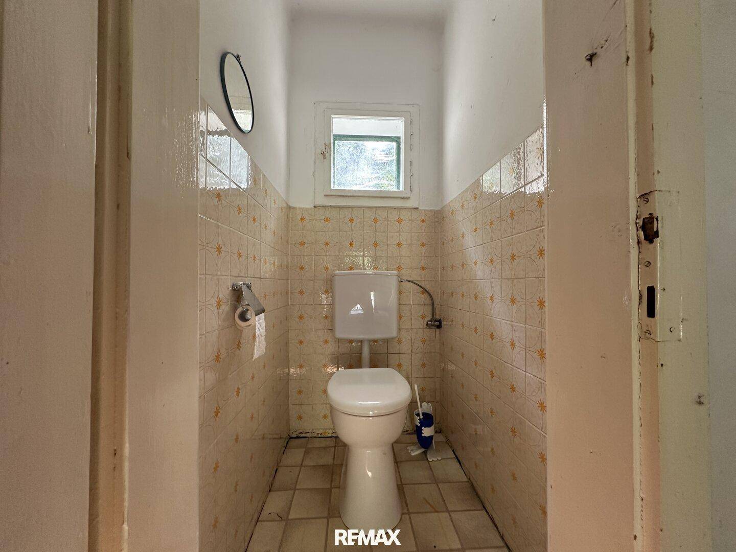 Kleines WC mit Fenster, traditionellen Fliesen und einfacher Toilette.