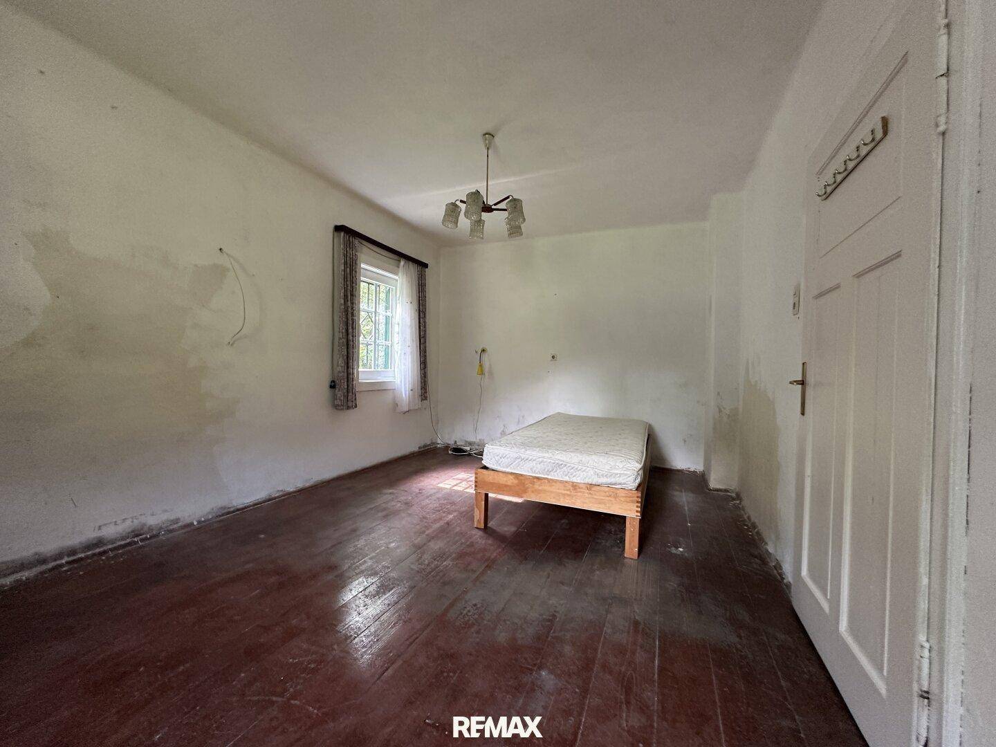 Schlafzimmer mit Holzboden, einem einfachen Bettgestell und einem Fenster.