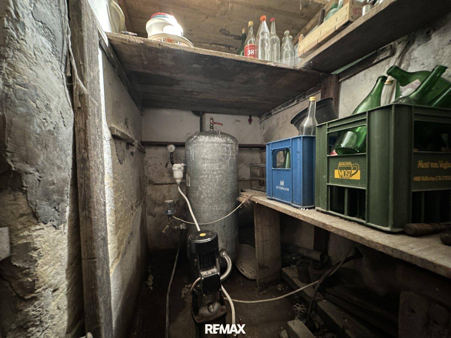 Kellerraum mit Wasserboiler, Regalen und unfertigen Wänden, dient als Abstellraum.